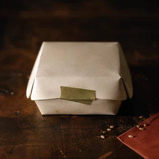 Caja para llevar sin marca cerrada con cinta verde sobre una barra de madera.