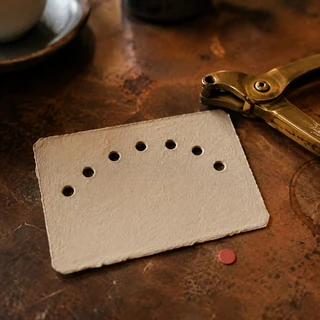 Tarjeta de fidelidad sin texto perforada a mano junto a una pinza de latón.